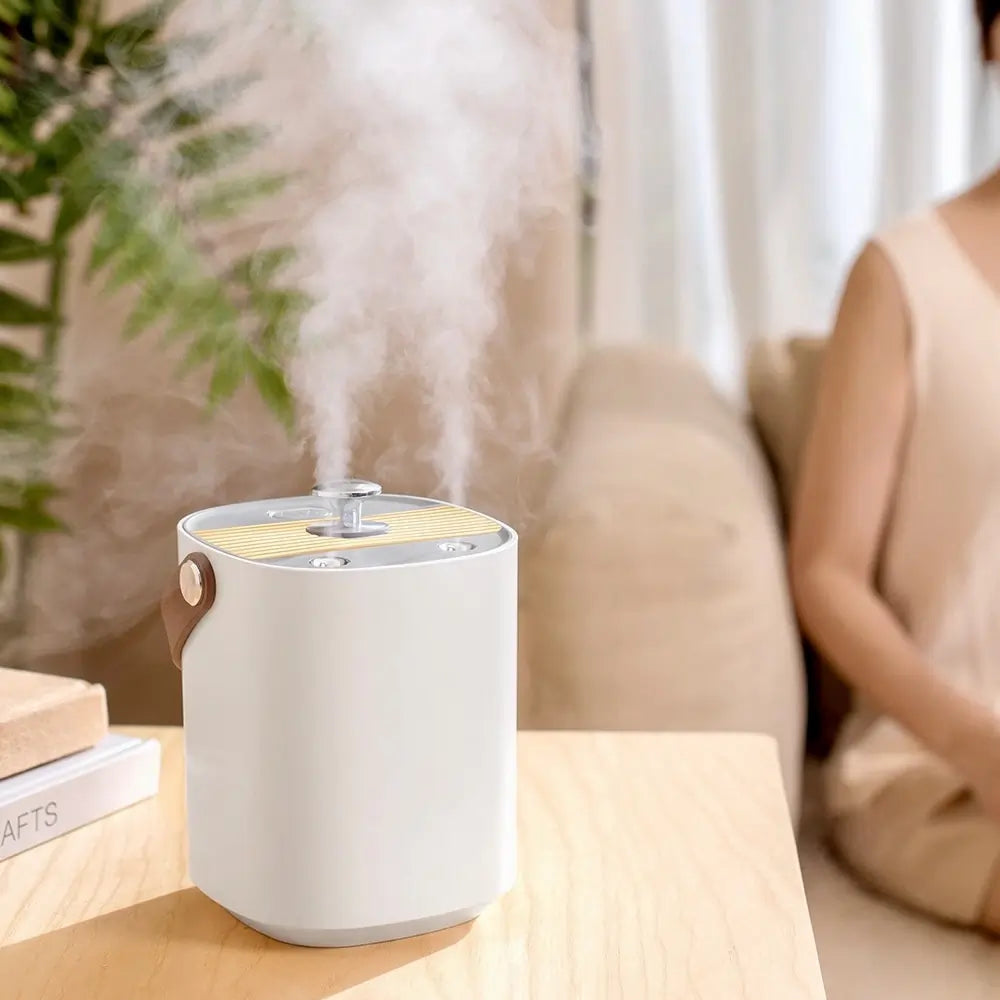 White humidifier on a wooden table with steam rising, woman sitting in the background